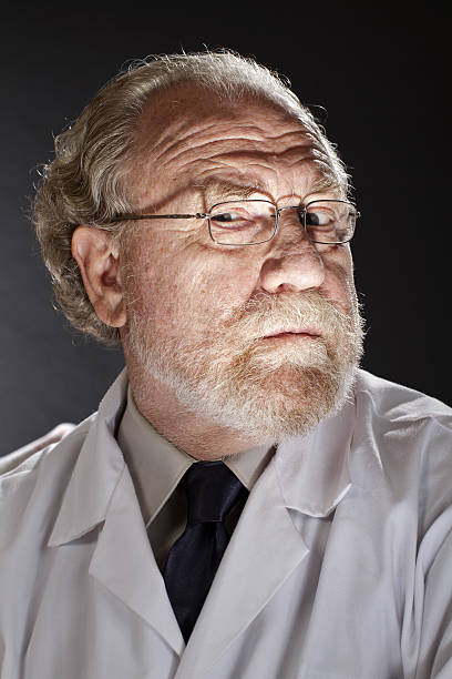 Portrait of evil doctor in lab coat and necktie with sinister expression. Dark background and dramatic low angle spot lighting create spooky shadows on face.